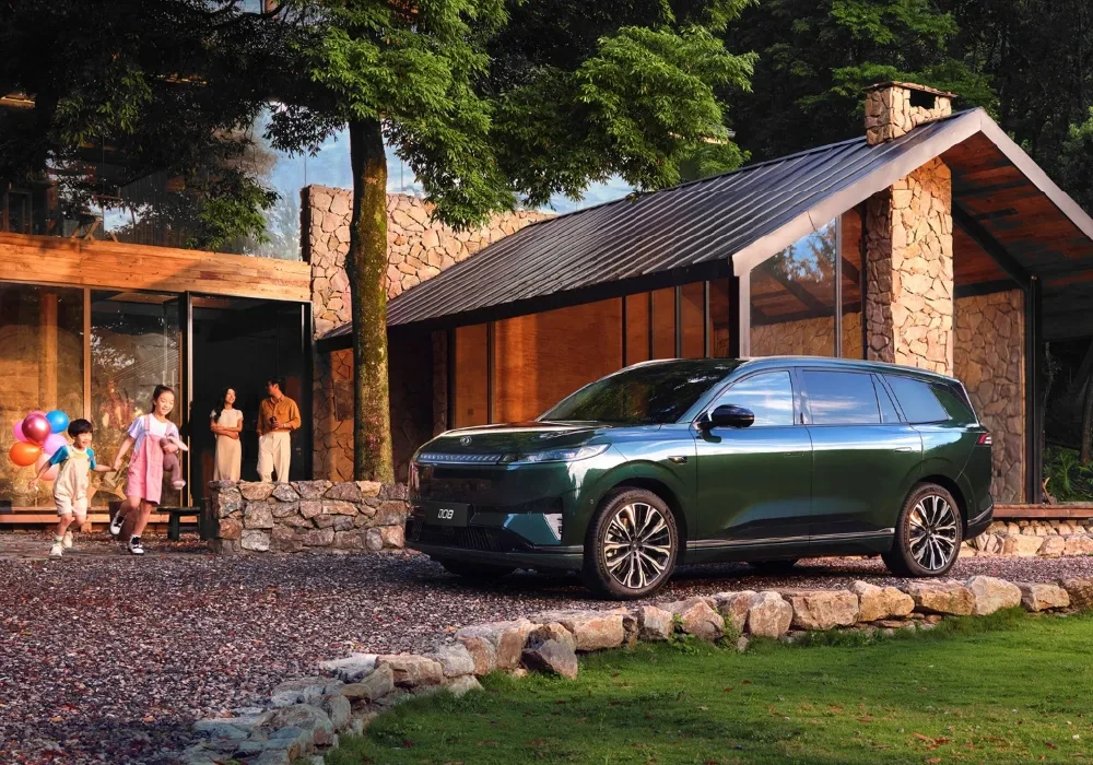 Dongfeng 008 verde junto a una casa entre árboles, con una familia